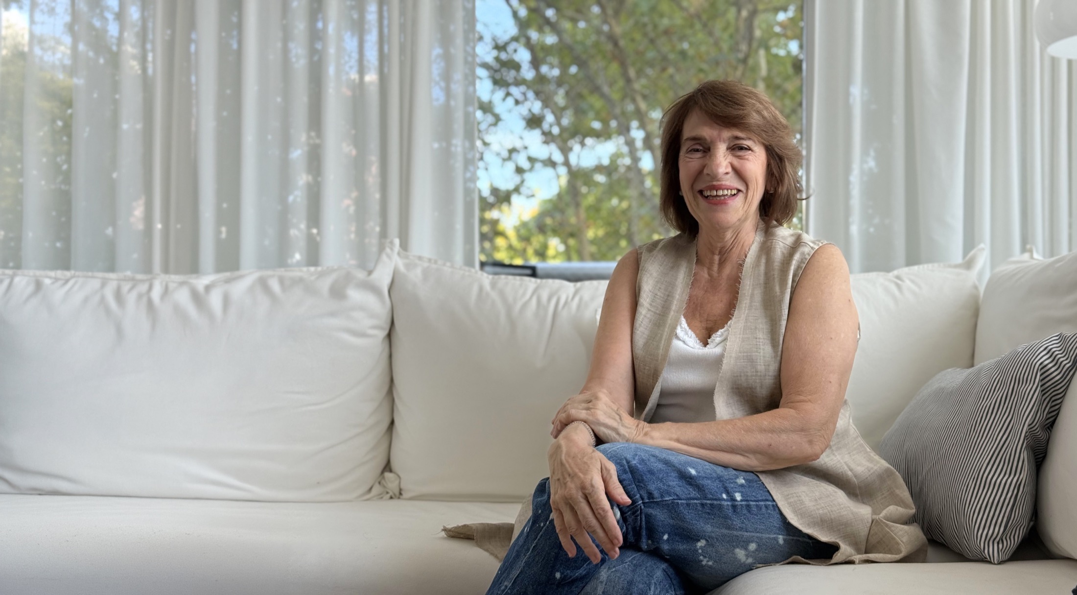 Anni Schuff sonriendo en su living, sentada en un sillón blanco